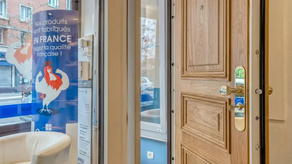 Entrée moderne d'une maison contemporaine avec porte d'entrée sécurisée ouverte, mur en briques apparentes beiges et façade blanche lisse