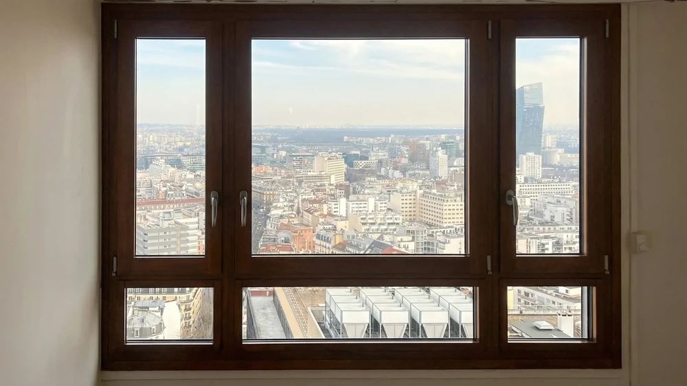 Intérieur moderne avec chaise design en tissu beige aux pieds en bois, positionnée devant grande baie vitrée donnant sur jardin