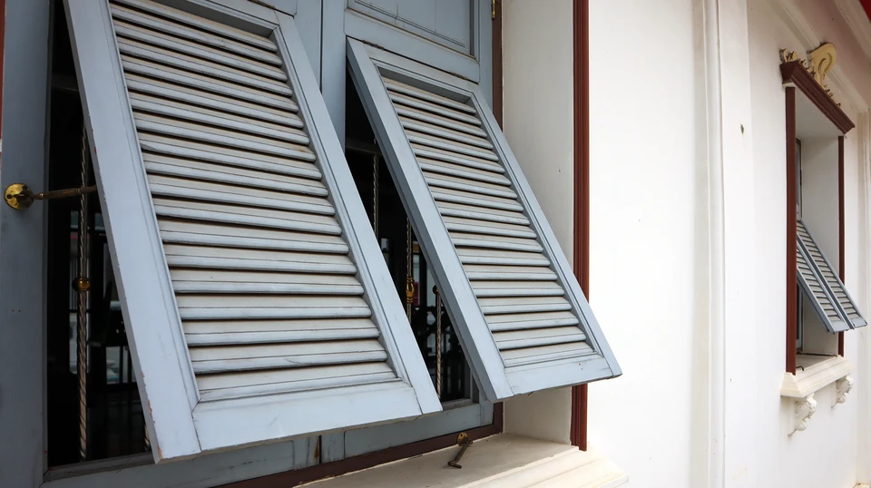 Façade méditerranéenne avec deux fenêtres ornées de volets en bois à persiennes rouges-bruns