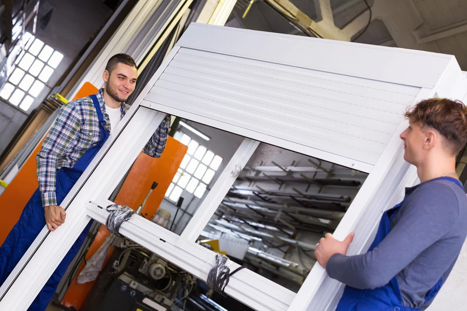 Atelier industriel avec technicien en polo rouge assemblant des profilés aluminium à l'aide d'une visseuse électrique