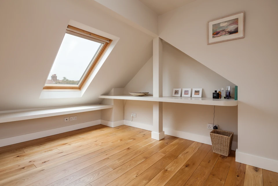 Chambre moderne sous combles avec lit blanc, coussins géométriques noirs et blancs, bureau en bois avec chaise grise, horloge murale, échelle décorative, suspension en rotin