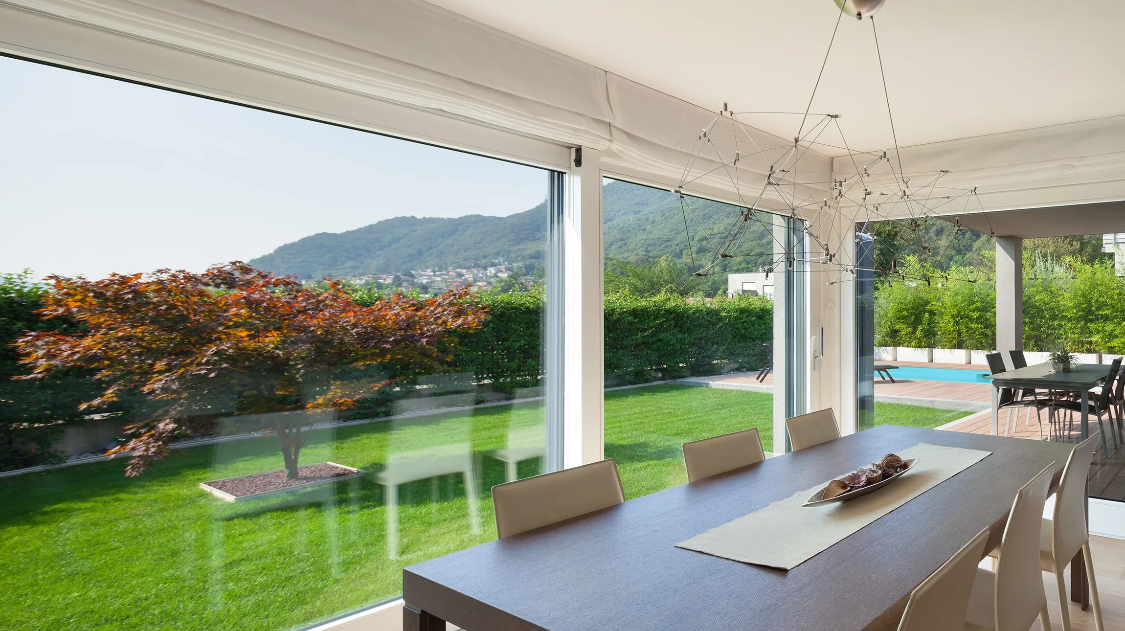 Salle à manger moderne avec grande baie vitrée coulissante ouvrant sur jardin paysager et piscine